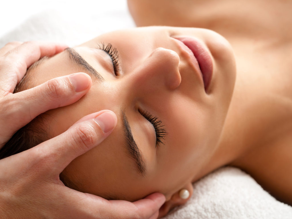 Close up head shot  of Woman having curative facial massage. Therapist applying pressure with thumbs on forehead.